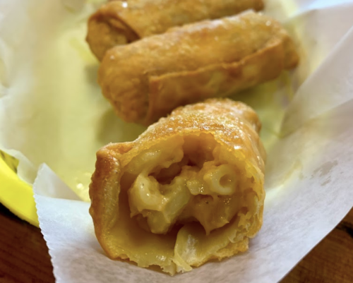 Fried spring rolls filled with creamy macaroni and cheese, served on a paper-lined plate.
