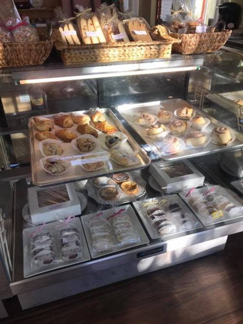 A display case filled with various baked goods, including pastries, cookies, and cinnamon rolls, under warm lighting.