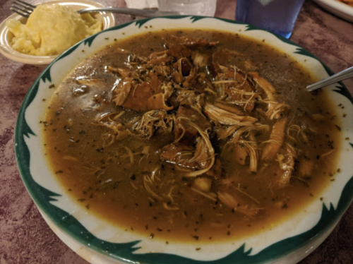 A bowl of savory chicken soup with shredded meat and herbs, served with a side of mashed potatoes.