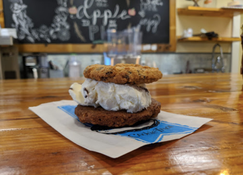 A cookie ice cream sandwich on a napkin, resting on a wooden counter in a cozy café.