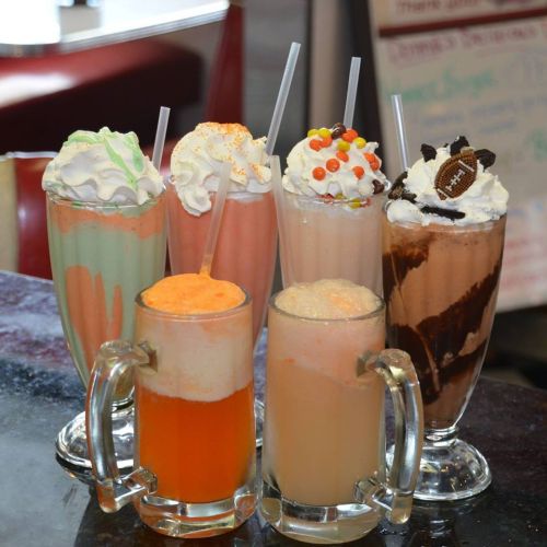 A colorful assortment of milkshakes topped with whipped cream, sprinkles, and candy, served in tall glasses.