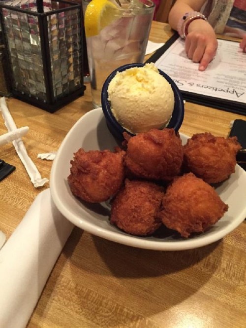 A bowl of golden-brown fried balls next to a scoop of vanilla ice cream on a wooden table.