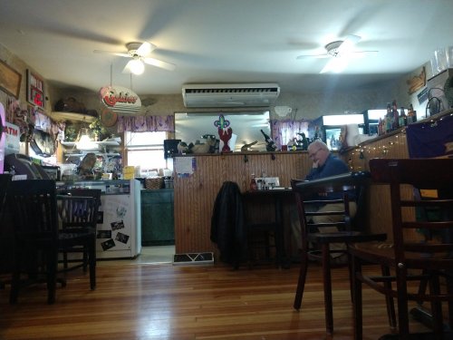 A cozy restaurant interior with wooden floors, a man sitting at a table, and various decorations on the walls.