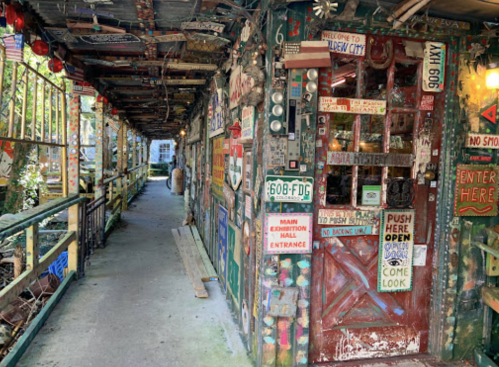 Colorful hallway adorned with eclectic signs and decorations, leading to a wooden door marked "Enter Here."