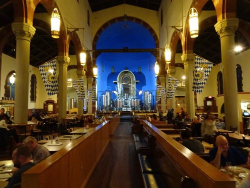 Interior of a spacious restaurant with blue walls, tall arches, and festive decorations, filled with diners.