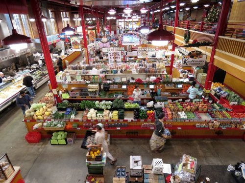 A bustling market filled with colorful fruits and vegetables, shoppers browsing stalls under bright lights.