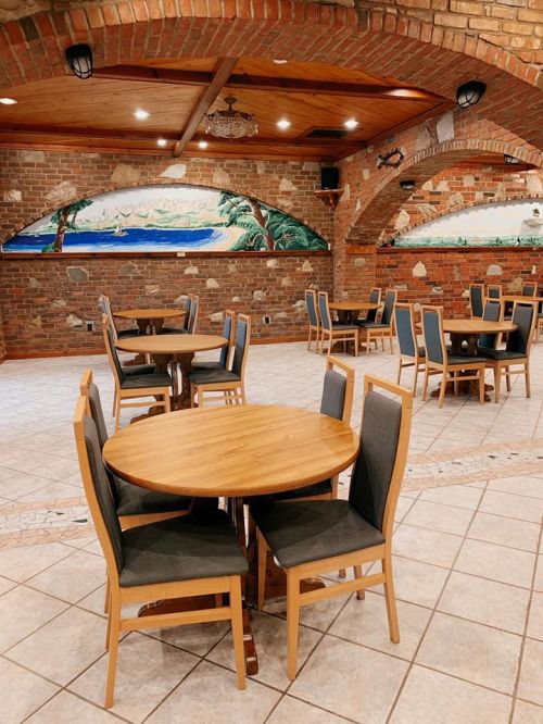 A spacious restaurant interior with wooden tables and chairs, featuring brick arches and mural artwork on the walls.