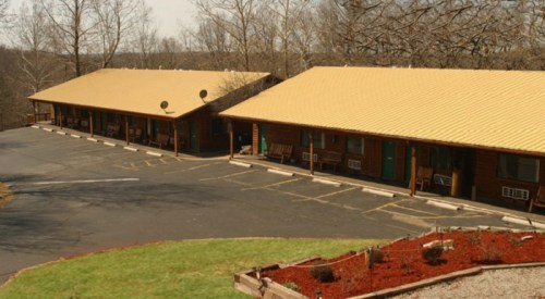 A row of rustic cabins with yellow roofs, surrounded by trees and a landscaped area, on a paved driveway.