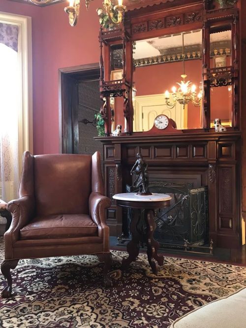 A cozy room featuring a leather armchair, ornate mirror, fireplace, and decorative table on a patterned rug.