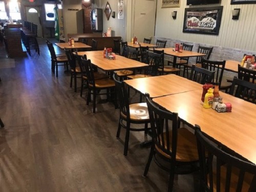 Interior of a restaurant with empty tables, chairs, and condiments on the tables, featuring a warm, inviting atmosphere.