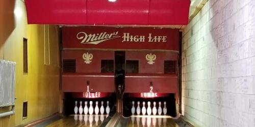 Bowling alley with two lanes, featuring a vintage Miller High Life sign and neatly arranged bowling pins.