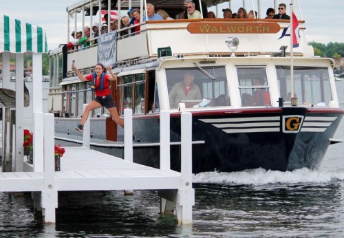 A woman jumps from a dock as a boat named "Walworth" approaches, with passengers watching from the deck.