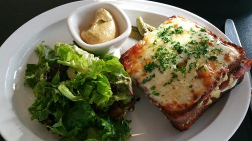 A plate featuring a cheesy sandwich, a side of mustard, pickles, and a fresh green salad.