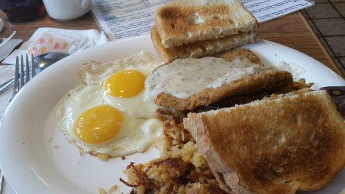 A plate of breakfast featuring two eggs, chicken fried steak with gravy, hash browns, and toasted bread.