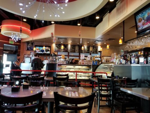 Interior of a restaurant with tables, a dessert display, and a bar area, featuring modern decor and a TV screen.