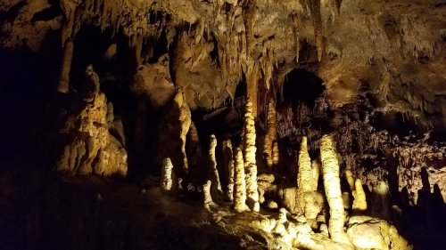 Stalactites and stalagmites illuminated in a dark cave, showcasing unique rock formations.