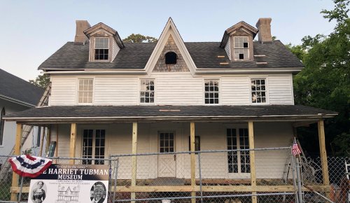 Historic house under renovation, featuring a sign for the Harriet Tubman Museum and a fenced area with American flags.