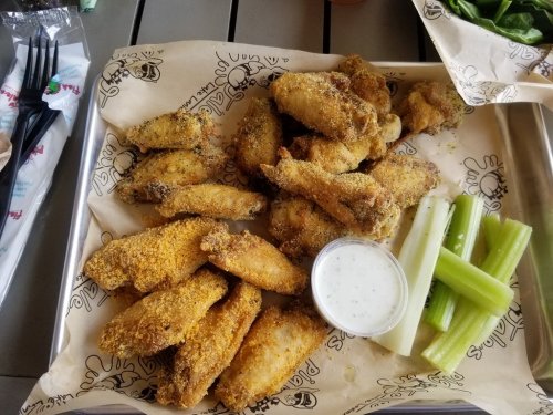 A tray of crispy chicken wings with a side of celery sticks and ranch dressing.