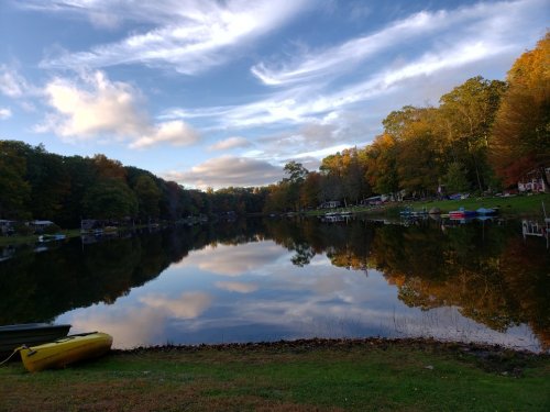 A serene lake surrounded by autumn trees, reflecting clouds and colorful foliage, with boats along the shore.