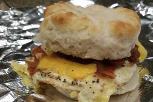 A biscuit sandwich with bacon, a fried egg, and melted cheese, wrapped in foil.