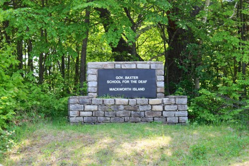 Sign for Gov. Baxter School for the Deaf, located on Mackworth Island, surrounded by greenery.