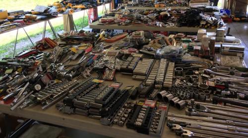 A large assortment of tools and hardware spread across multiple tables, including wrenches, sockets, and various accessories.