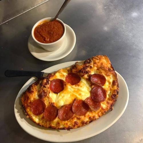 A cheesy pepperoni pizza on a plate, accompanied by a bowl of marinara sauce.