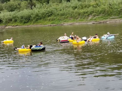 A group of people floating on colorful inner tubes in a calm river, surrounded by greenery.
