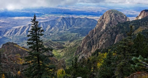 A panoramic view of rugged mountains and valleys, with lush greenery and a cloudy sky in the background.