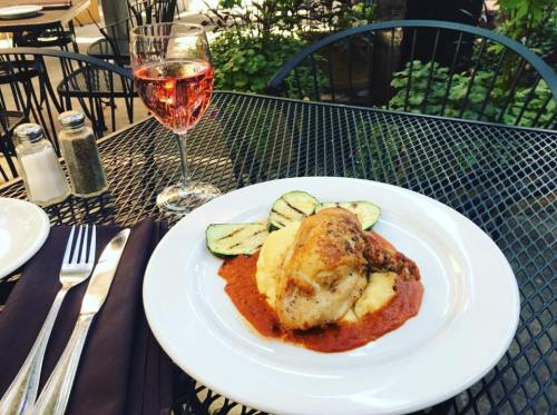 A plate of chicken with sauce and zucchini, served with mashed potatoes, alongside a glass of rosé wine on a table.