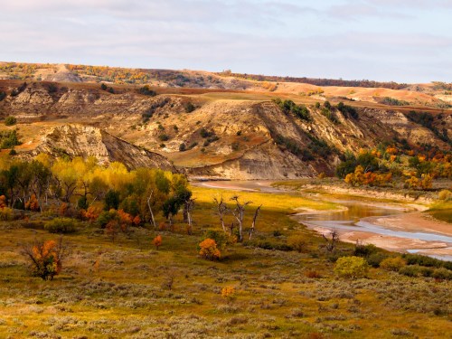 A scenic landscape featuring rolling hills, autumn foliage, and a winding river under a cloudy sky.