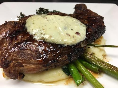 A juicy steak topped with herb butter, served on a bed of mashed potatoes and garnished with green onions.