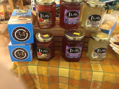 A display of jars with various jams and jellies, alongside boxes of vanilla cake mix on a checkered tablecloth.