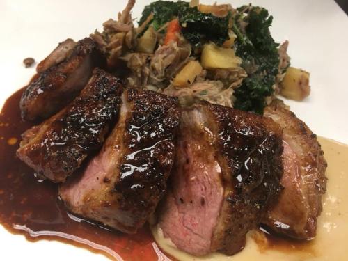 Sliced seared duck breast with a glossy sauce, served alongside pulled meat and sautéed greens with apples.