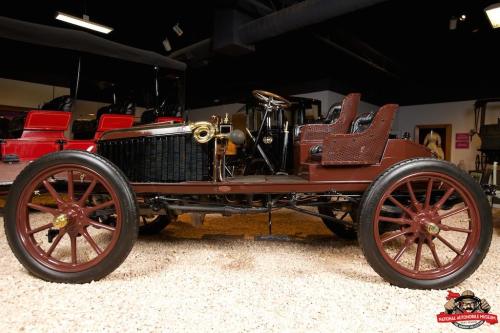 A vintage automobile displayed in a museum, featuring a brown body and wooden wheels, showcasing early 20th-century design.