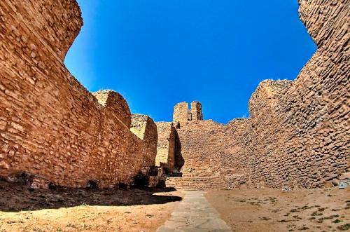 Ruins of an ancient stone structure under a clear blue sky, with walls and a tower visible in the background.