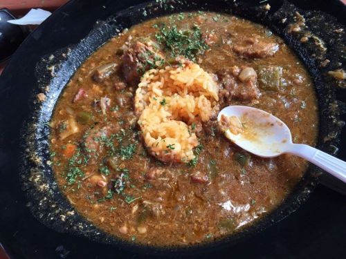 A plate of flavorful stew with rice in the center, garnished with herbs, served in a black dish.