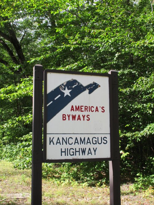 Sign for Kancamagus Highway, part of America's Byways, surrounded by lush green trees.