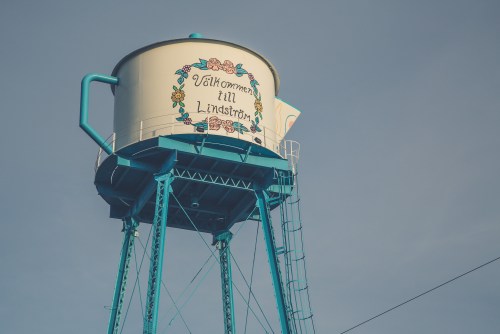 A blue water tower with "Välkommen till Lindström" painted on it, surrounded by decorative floral designs.