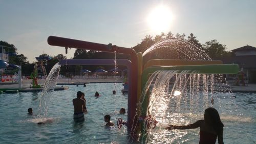 Children play in a pool with colorful water features, splashing under a bright sun.