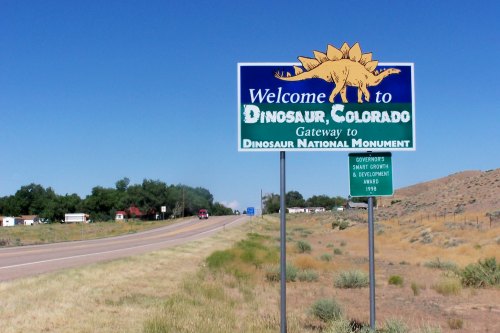 Welcome sign for Dinosaur, Colorado, marking the gateway to Dinosaur National Monument against a clear blue sky.