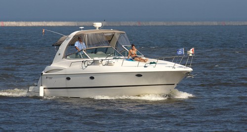 A white motorboat with two people on board cruising through calm waters on a sunny day.