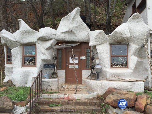 A unique, textured white house with rocky features, surrounded by greenery and wooden accents.