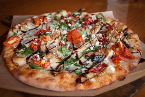 A delicious pizza topped with grilled chicken, spinach, sun-dried tomatoes, and drizzled with balsamic glaze.