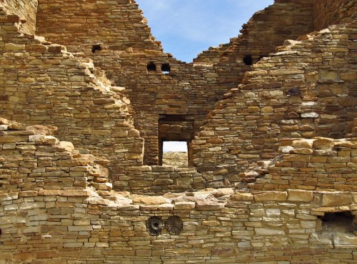 Ruins of an ancient stone structure with openings and textured walls under a blue sky.