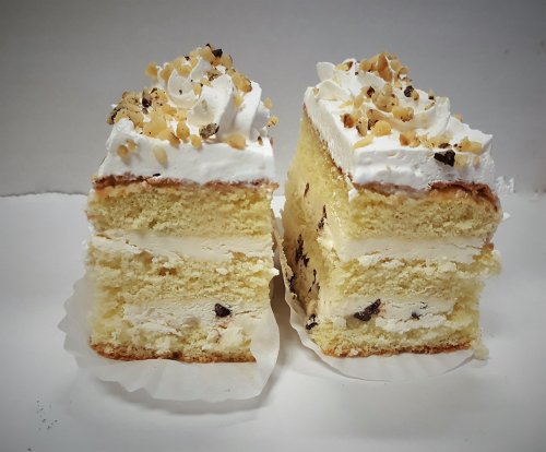 Two slices of layered cake with whipped cream and chopped nuts on top, showcasing creamy filling and light sponge layers.