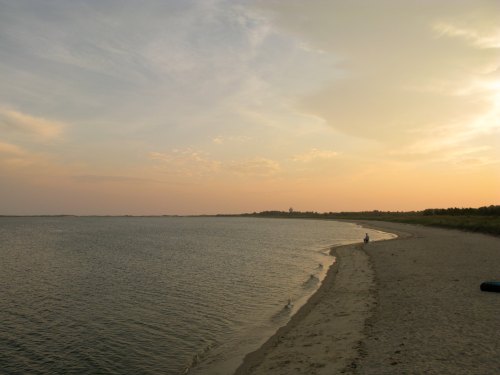 A serene beach at sunset, with gentle waves lapping the shore and a person walking along the sandy coastline.