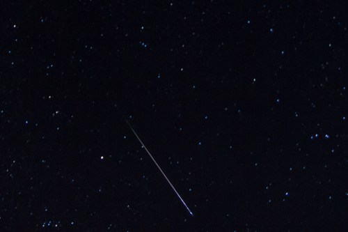 A night sky filled with stars, featuring a bright meteor streaking across the scene.