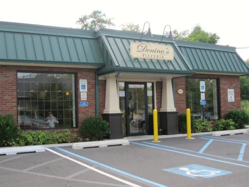 Exterior of Denino's Pizzeria, featuring a brick facade, green roof, and accessible parking spaces.
