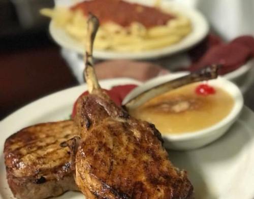 A plate featuring grilled pork chops, a side of applesauce, and a dish of pasta with red sauce in the background.